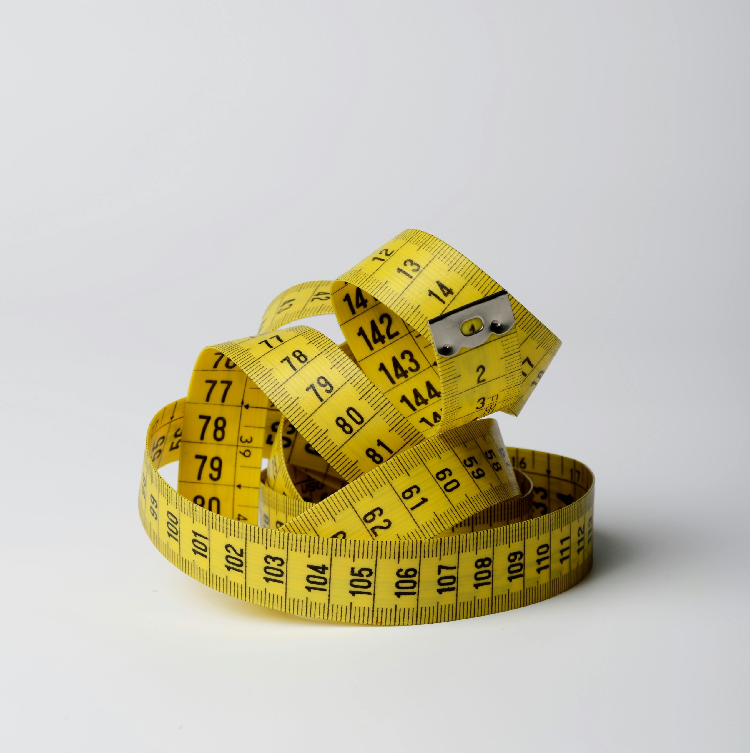 A bright yellow measuring tape coiled in loops, showcasing measurements clearly against a white background.