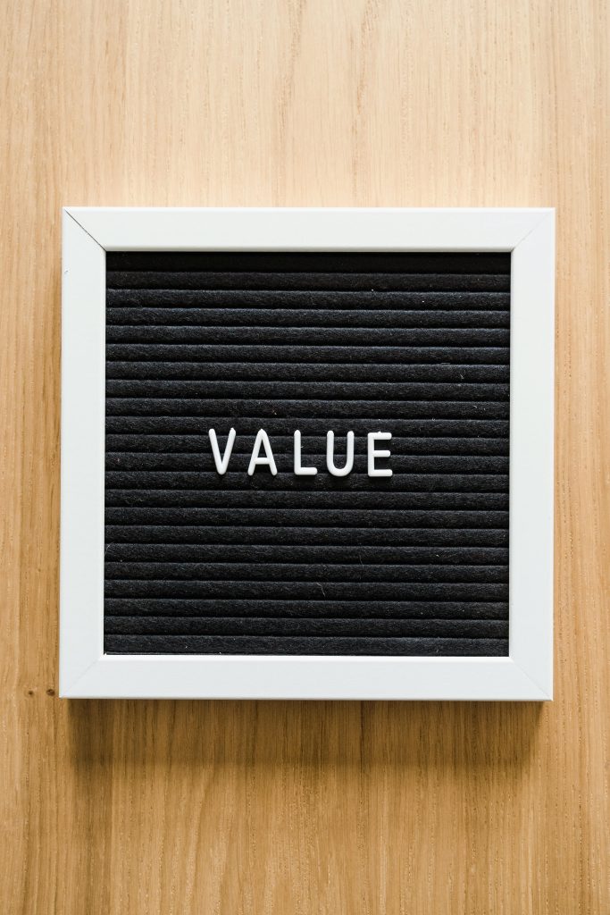 A black felt board reading 'VALUE' framed in white, set against a wooden backdrop. Ideal for business concepts.